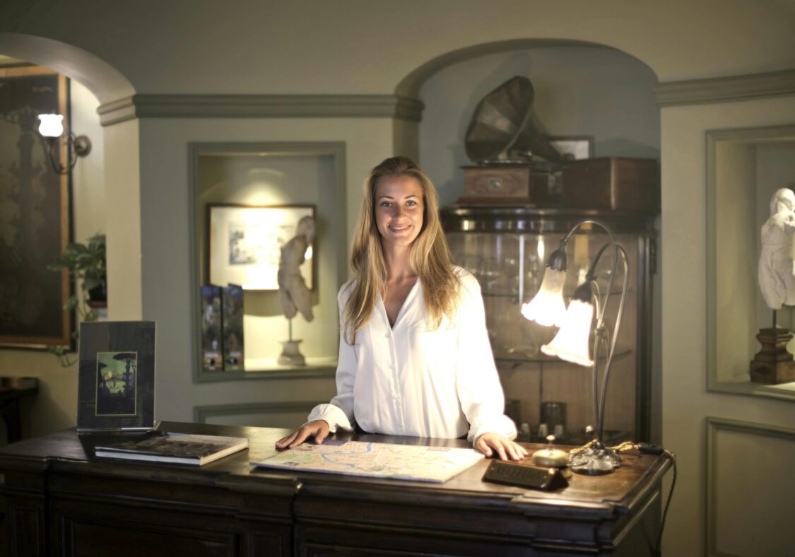 Caucasian woman smiling behind hotel reception desk, creating a warm and welcoming atmosphere.